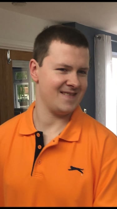 A photo of a young man smiling and wearing an orange polo shirt